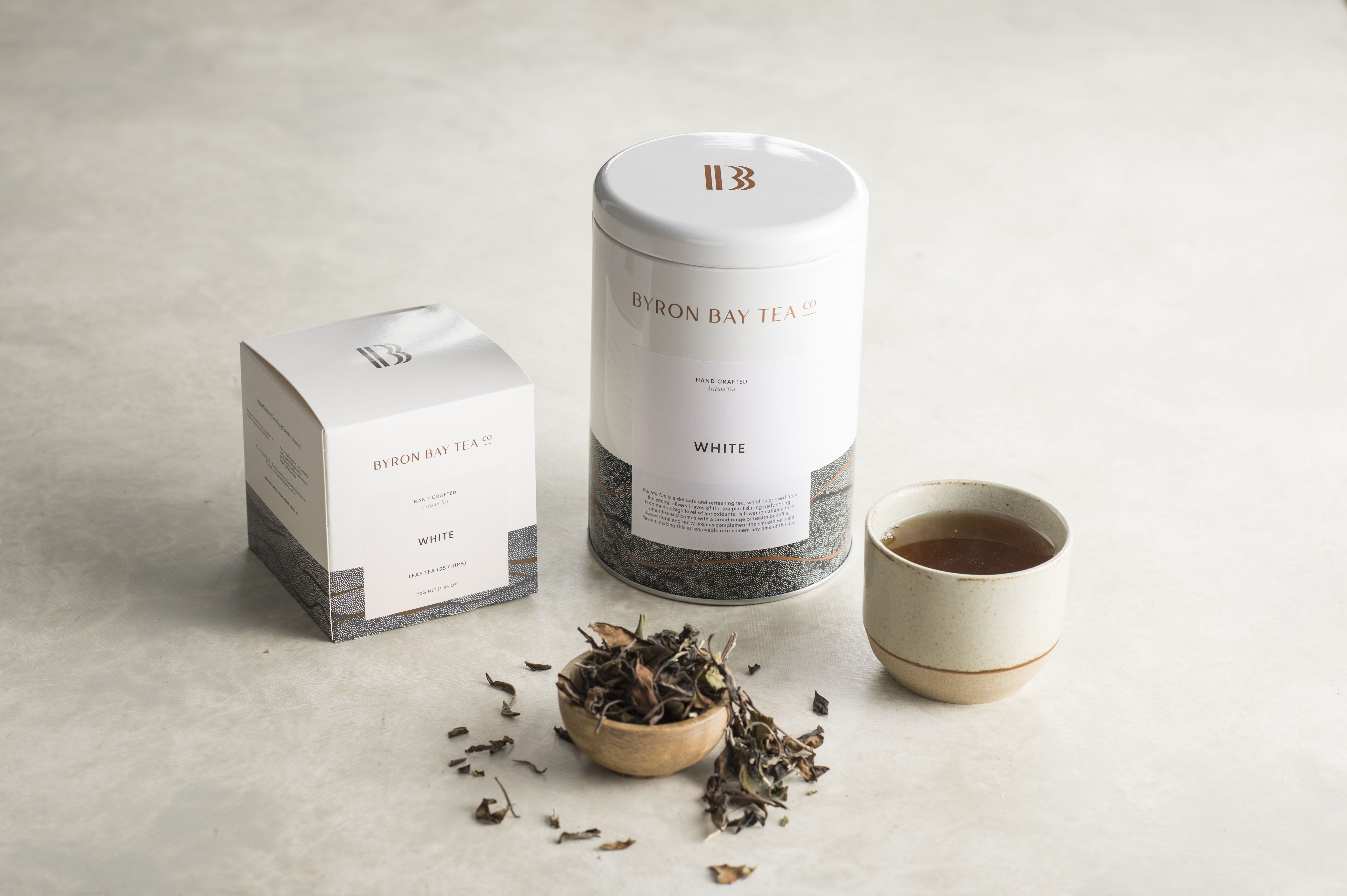 byron bay tea company white tea box and tin next to brewed cup of white tea on polished concrete