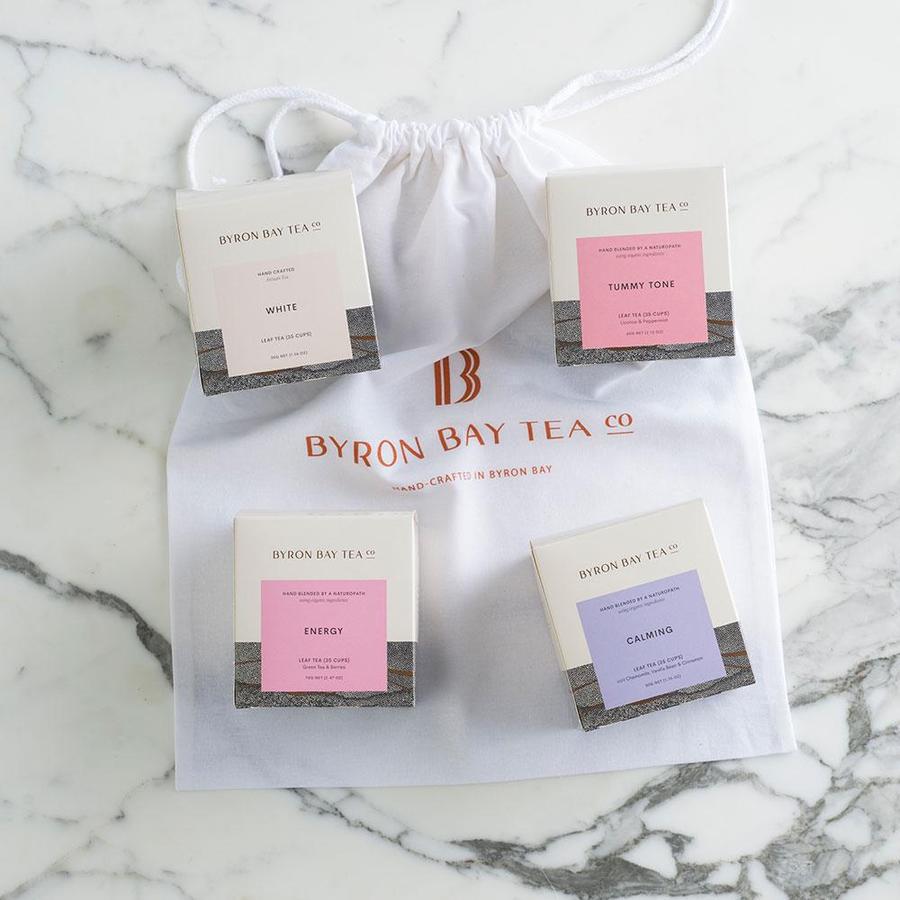 byron bay tea company byron bliss collection containing boxes of white, tummy tone, energy and calming tea on white byron bay tea company drawstring bag on marble background