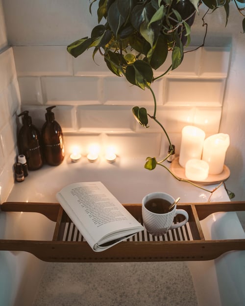 Book and cup of tea resting on bath as candles are lit